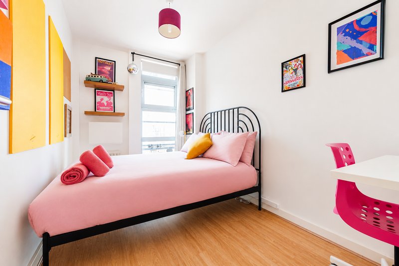 Bright children's bedroom with pink bed, yellow door, framed art, and wooden floor