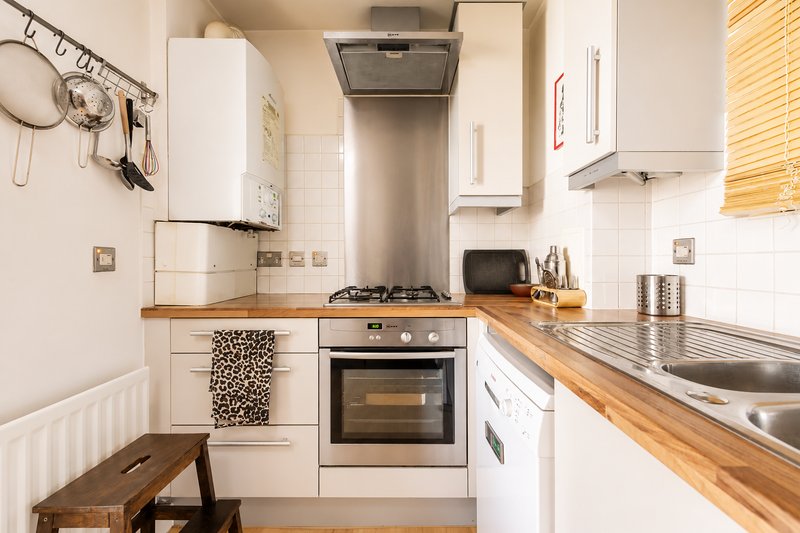 Compact kitchen with white cabinetry, wooden countertops, stainless steel appliances and small dining bench