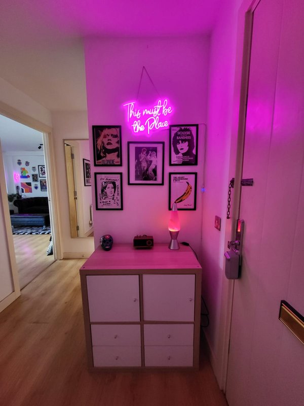 Magenta-lit entryway with neon sign, framed artwork, and pink storage unit