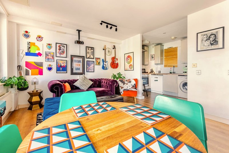 Open-plan living room with colorful wall art, purple velvet sofa, wooden dining table and turquoise chairs