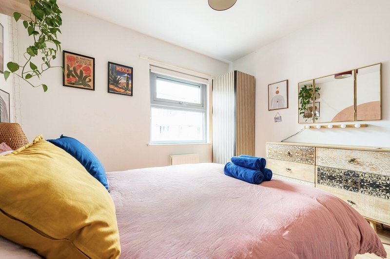 Bright bedroom with double bed, yellow and blue pillows, wooden dresser and wall art