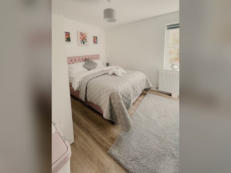 Bedroom with double bed, pink headboard, wooden floor, and window with radiator