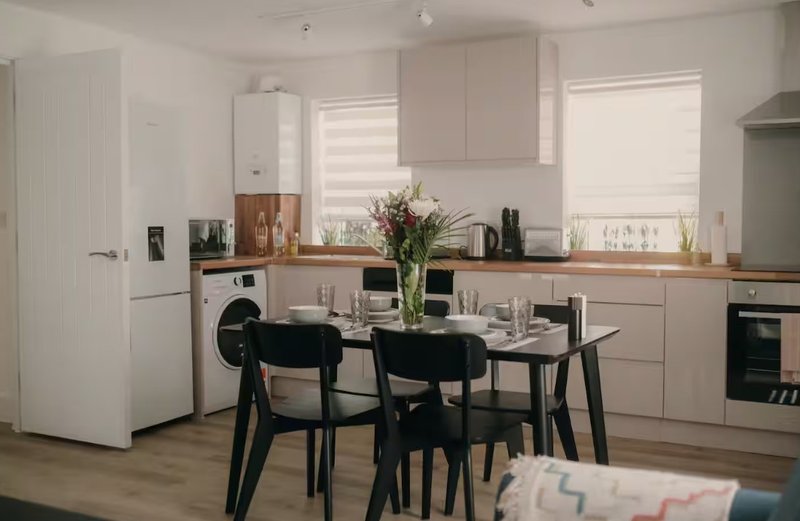 Modern kitchen with dining table, black chairs, wooden countertops and white cabinetry
