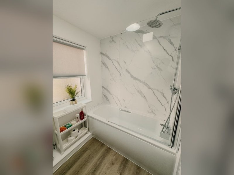 Modern bathroom with marble-effect tiles, white bathtub, rainfall showerhead, and floating shelves