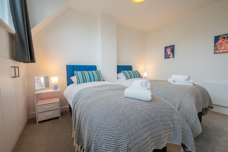 Bright bedroom with two single beds, blue headboards, striped pillows and white towels