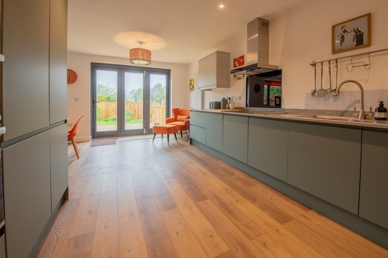 Modern kitchen with sage cabinetry, wooden flooring, island seating and garden view doors