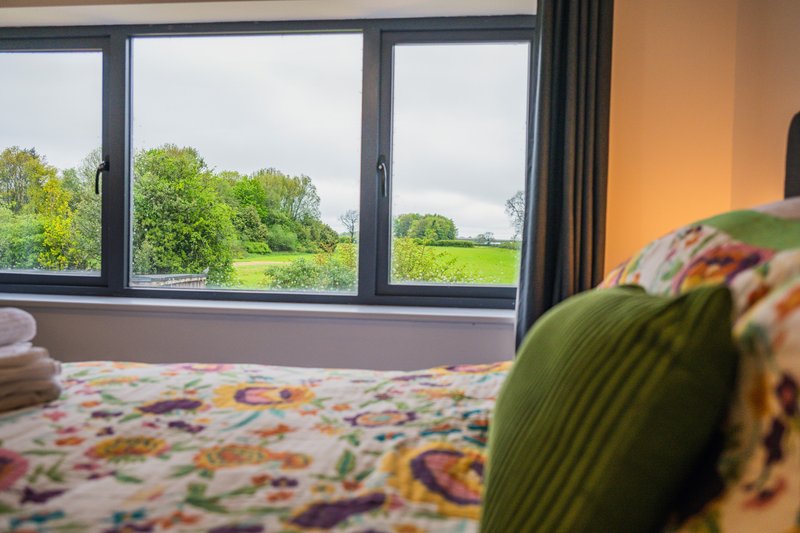 Bedroom with patterned bedding and large windows overlooking green countryside landscape