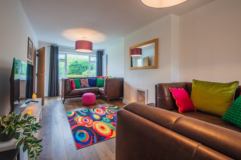 Bright living room with brown leather sofas, colorful geometric rug, and large windows with garden view
