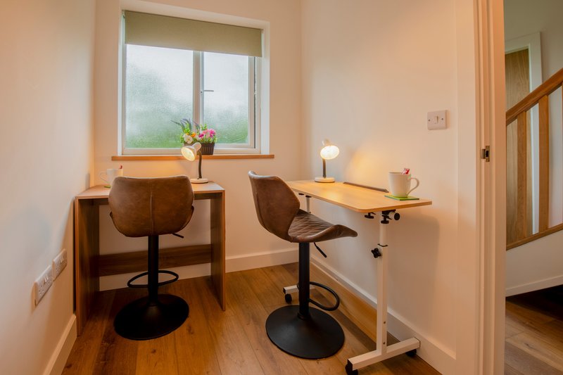 Home office with two brown leather chairs, wooden desk, window with countryside view, and wooden flooring