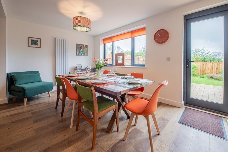Modern dining room with wooden table, orange and green chairs, teal sofa, and garden view