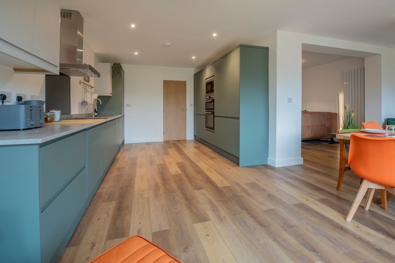 Open-plan kitchen and living area with teal cabinetry, wooden flooring, and modern furnishings