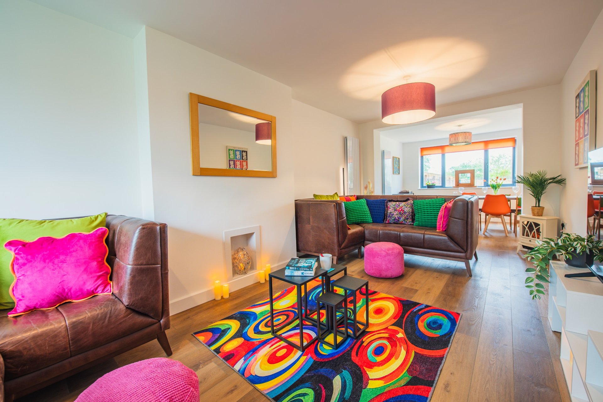 Bright open-plan living room with colorful rug, brown leather seating, and vibrant cushions