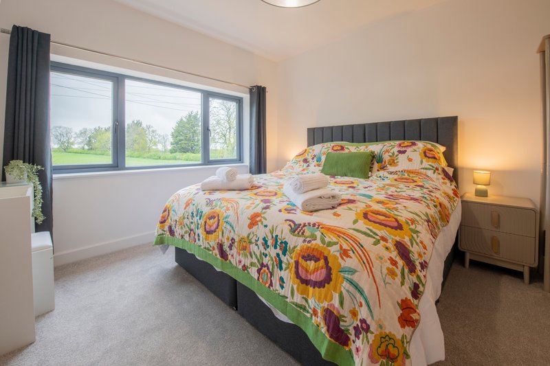 Bright bedroom with double bed, colorful patterned bedding, large windows and wooden furniture