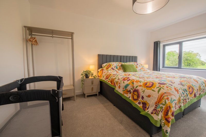 Bright bedroom with double bed, colorful bedding, wooden wardrobe, and garden views from window