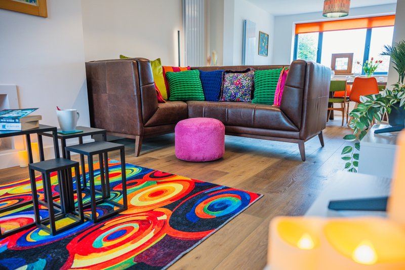 Colorful living room with brown leather sofa, bright rug, pink ottoman and modern furnishings