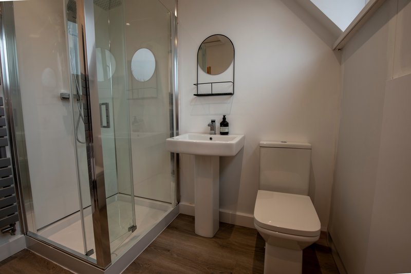 Modern bathroom with walk-in shower, pedestal sink, toilet and round mirror