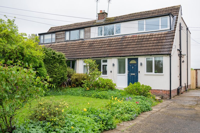 Semi-detached house with driveway, front garden, and overgrown landscaping