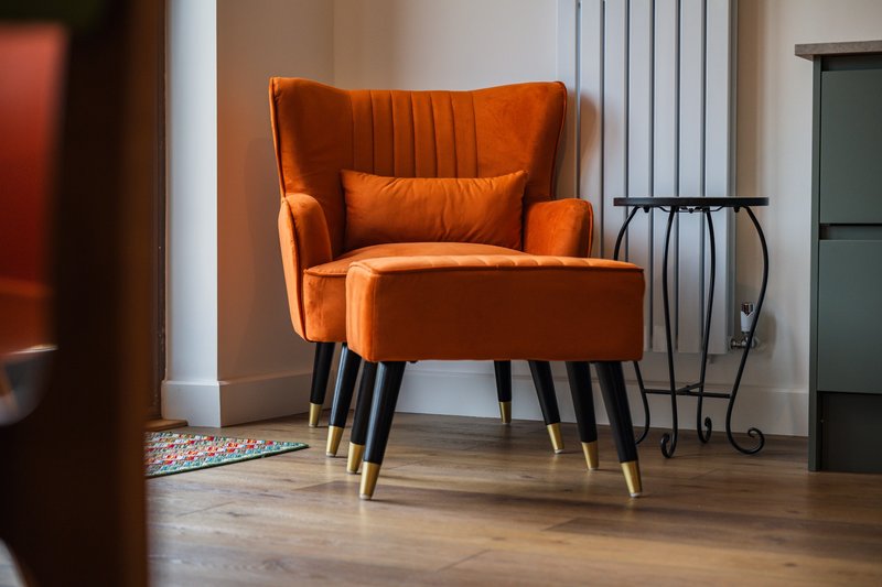 Orange upholstered wingback armchair with footstool and wooden legs in modern living room