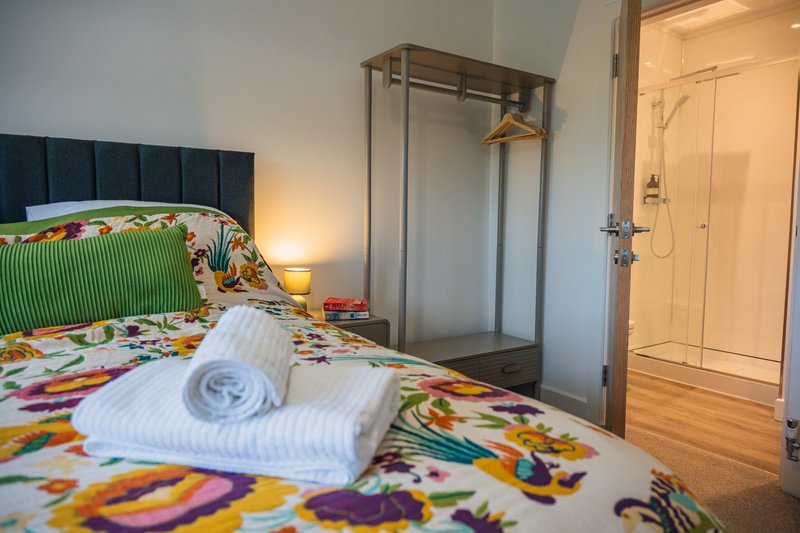 Bright bedroom with colorful bedding, rolled towels, dark headboard and wardrobe