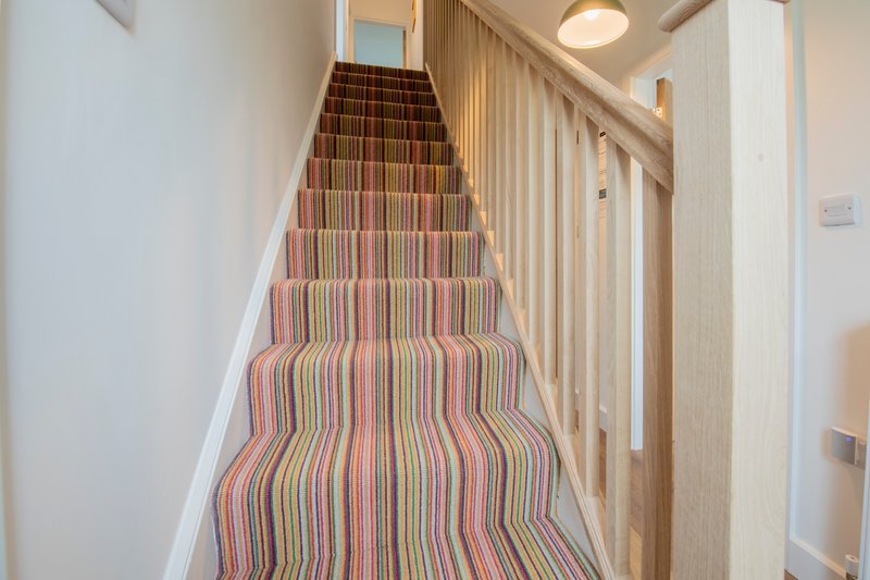 Staircase with striped carpet runner and wooden banister leading upward