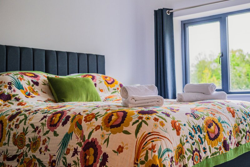 Bright bedroom with floral patterned bedding, green pillow, and blue-framed windows overlooking garden