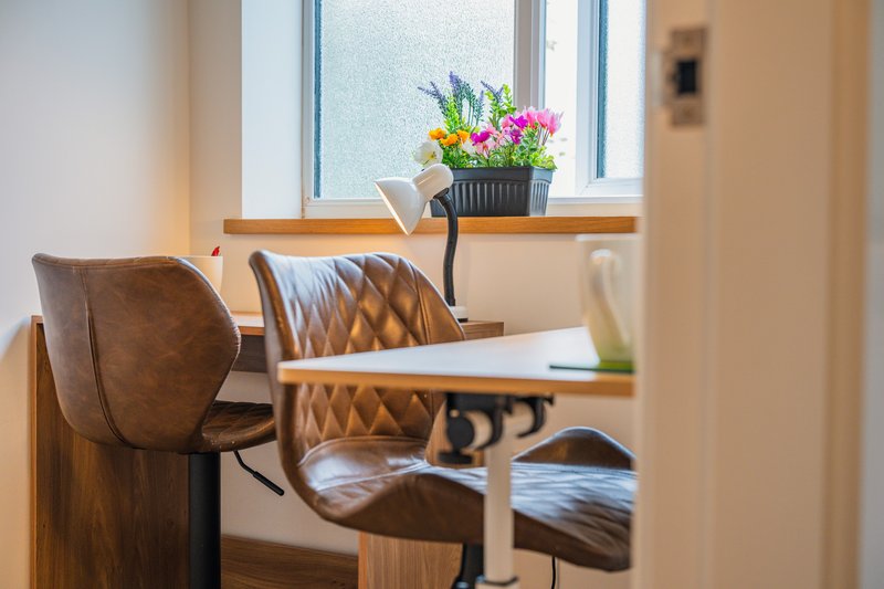 Modern home office with wooden desk, brown leather chair, potted flowers on windowsill
