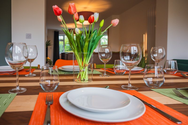 Dining table set for a meal with tulips, wine glasses, white plates and orange napkins