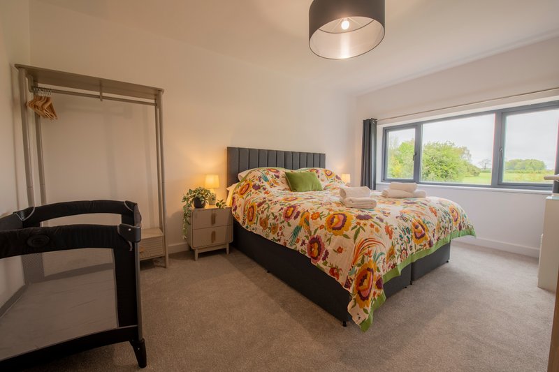 Bright bedroom with double bed, patterned bedding, pendant light and large windows