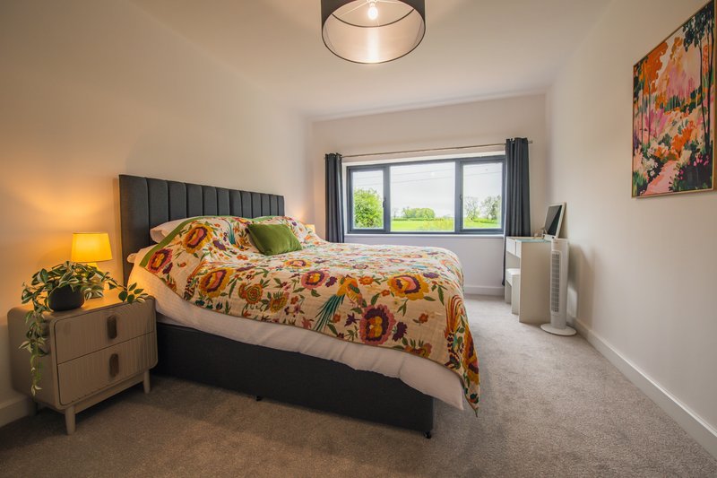 Bright bedroom with double bed, upholstered headboard, bedside lamp and window view