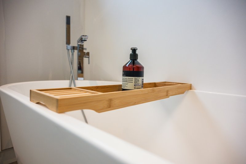 Modern white bathtub with wooden bath caddy holding faucet and toiletries