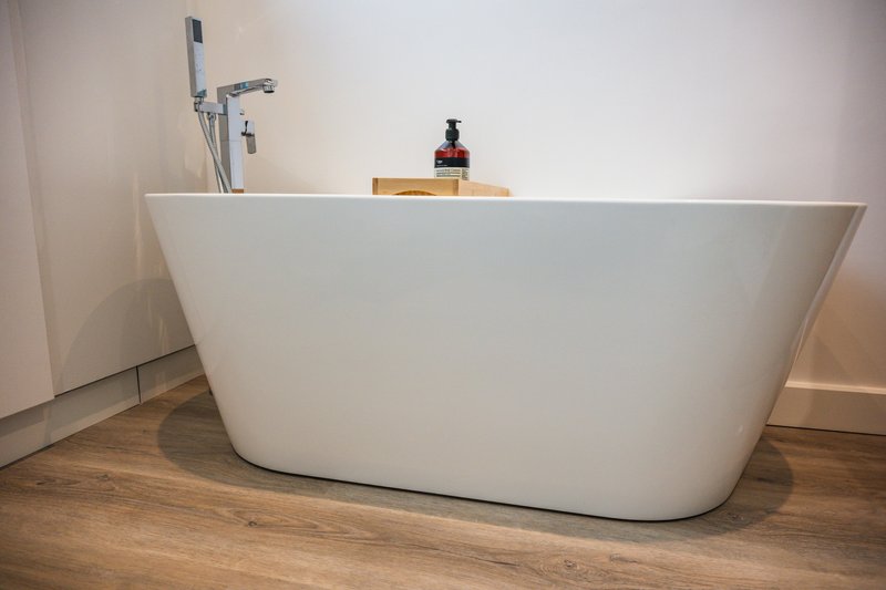 Modern white freestanding bathtub with chrome fixtures and wooden floor