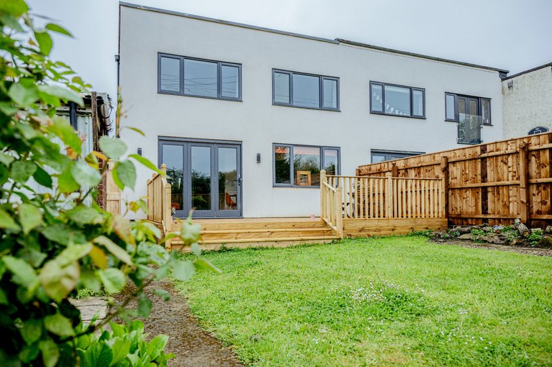 Modern house with wooden deck, fenced garden, and well-maintained lawn area