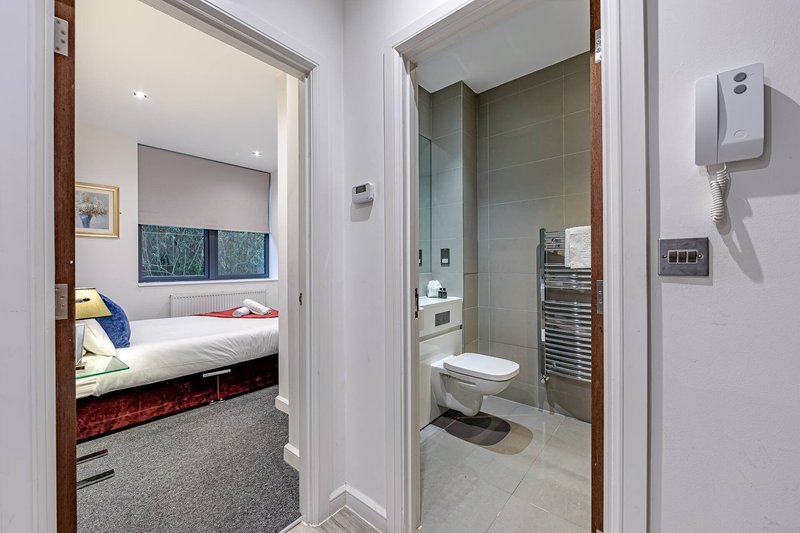 Hallway view showing modern bedroom with bed and bathroom with toilet, sink and heated towel rail