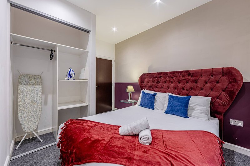 Modern bedroom with red upholstered headboard, white bedding, blue cushions, and built-in wardrobe