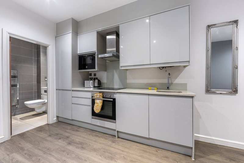 Modern kitchen with white cabinetry, integrated appliances, wooden flooring and bathroom visible through open door