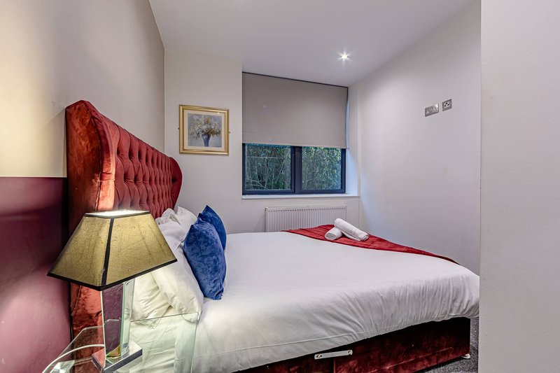 Modern bedroom with red upholstered headboard, white bedding, table lamp and framed wall art