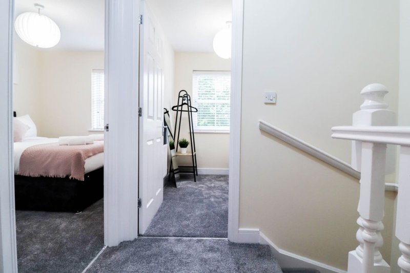 Hallway with open doors leading to bedroom and bathroom, carpeted floor, white walls and railings