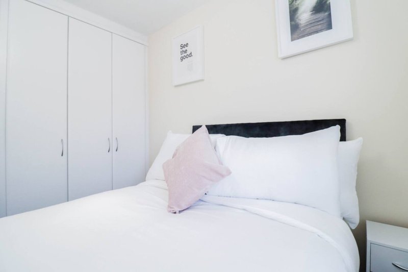 Bright bedroom with double bed, white bedding, pink cushion, black headboard, and built-in wardrobe