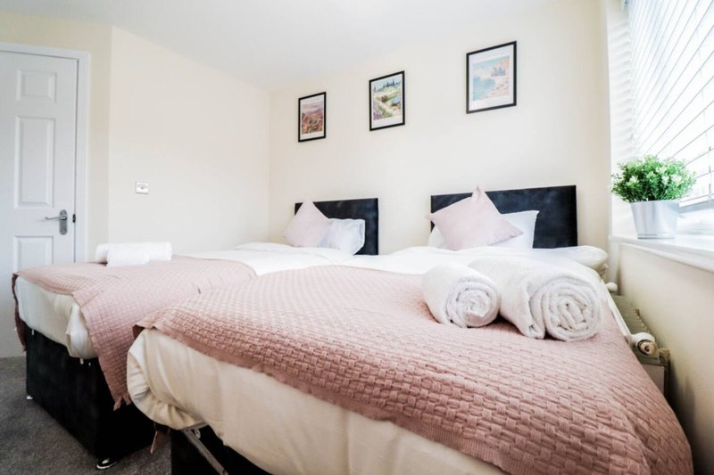 Bright bedroom with two single beds, pink quilts, white pillows and rolled towels
