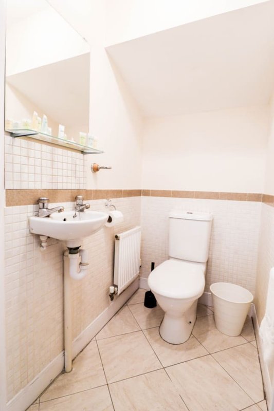 Small bathroom with white tile walls, beige floor, sink, toilet and radiator