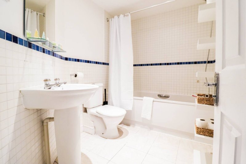 Clean bathroom with white tiles, pedestal sink, toilet, bathtub and shower curtain