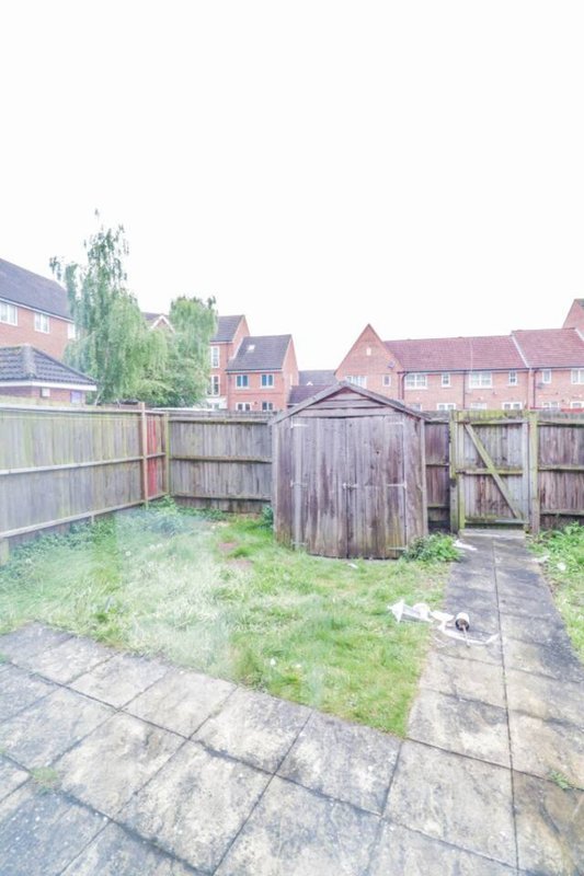 Residential garden with wooden fences, paved patio, and brick townhouses visible beyond