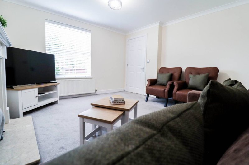 Bright living room with TV, dark sofas, wooden coffee tables and window