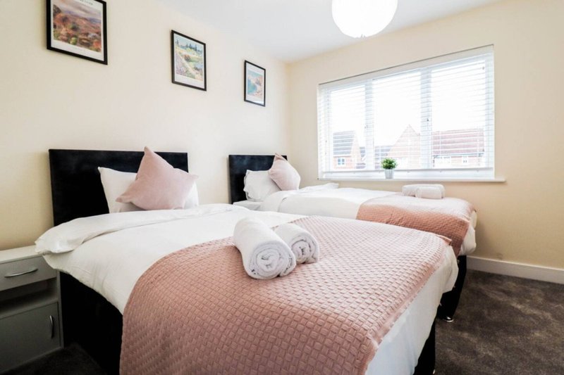 Twin bedroom with two single beds, pink bedding, black headboards and framed wall art