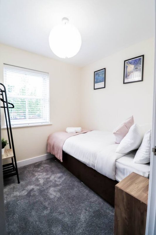 Small bedroom with single bed, white bedding, pink cushions, window and ceiling light