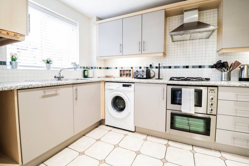 Modern kitchen with cream cabinets, white appliances, tiled floor and natural light from window