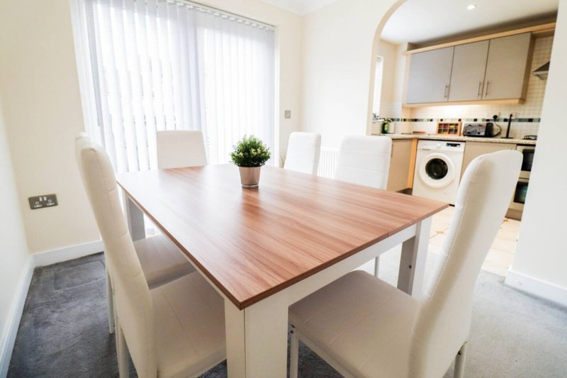 Modern kitchen-diner with wooden table, white chairs, and integrated appliances