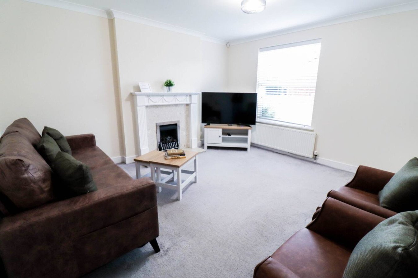 Living room with brown sofas, fireplace, TV, and bright window