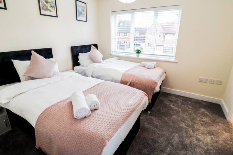Twin bedroom with two single beds, rolled towels, pink bedding, and large window overlooking street