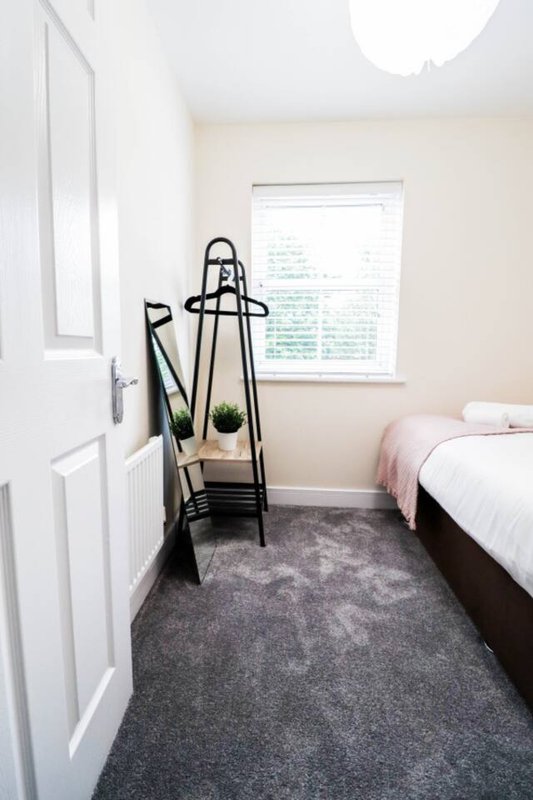 Bedroom corner with bed, window, coat stand and small potted plant on grey carpet